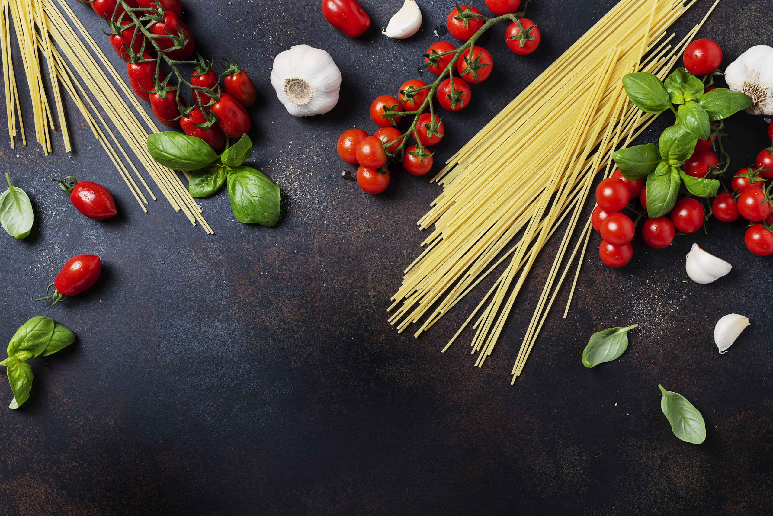 Ingredients for cooking italian pasta: spaghetti, tomato, basil and garlic on the black table. Top view image with a copy space